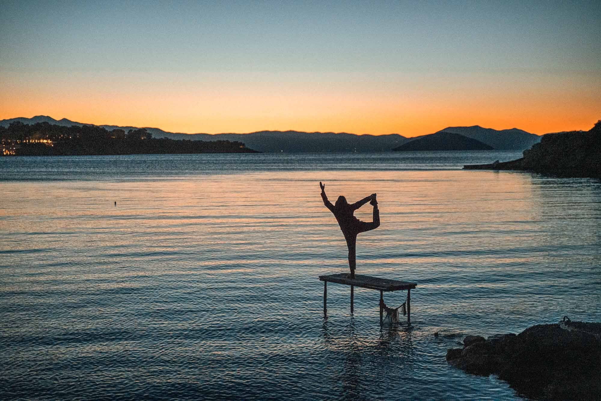 Yogapose auf einem steg in einer griechischen bucht beim sonnenuntergang
